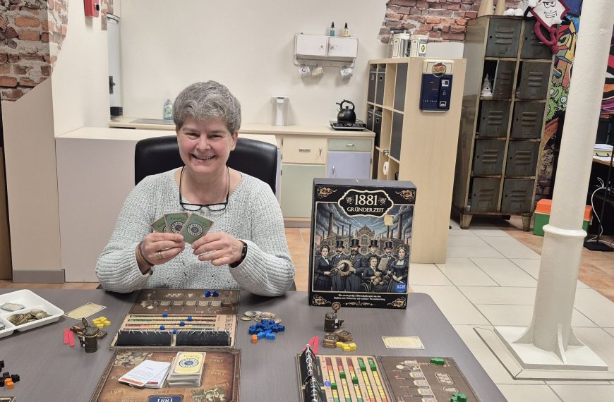 Frau sitzt an Tisch mit Spielmaterial.