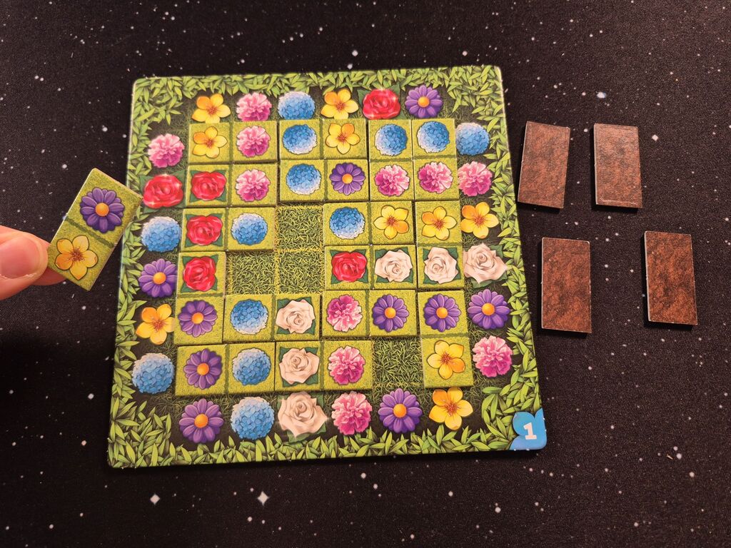 Hand hält Doppelplättchen über gefüllten Spielplan von "For One – Schwarze Rosen".