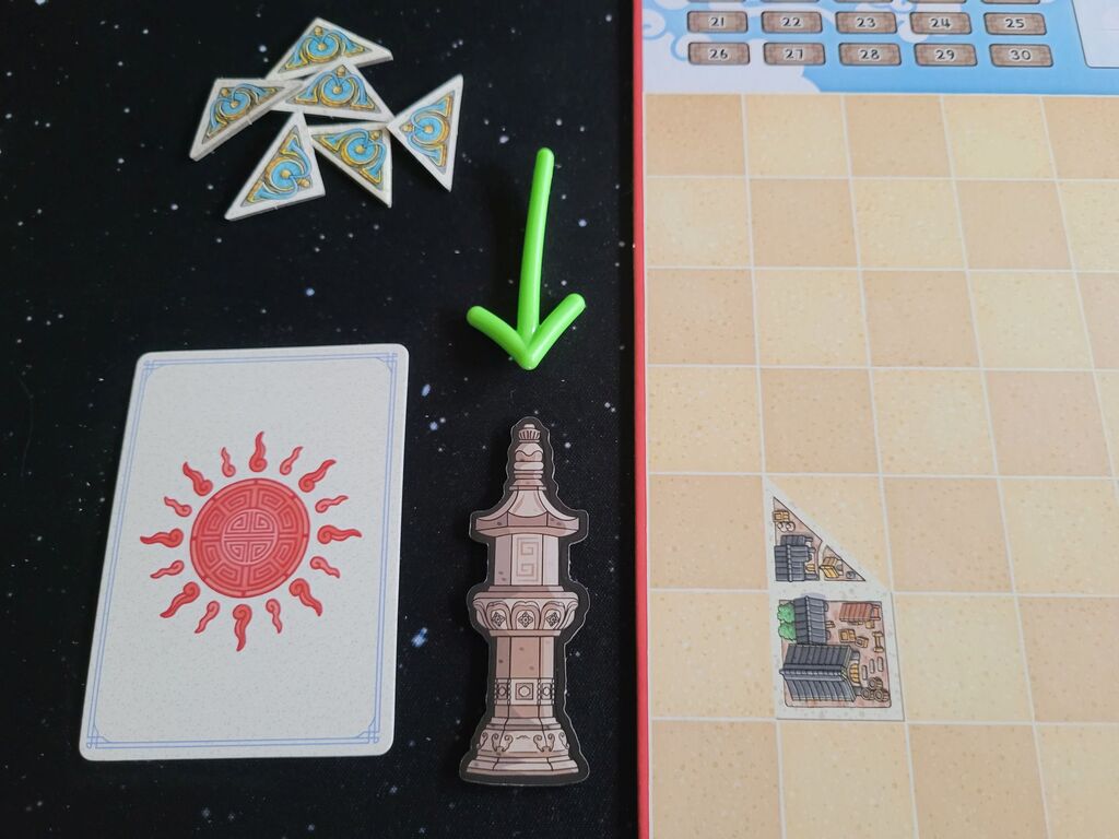 Zwischen Spielmaterial zeigt ein Pfeil auf einen Marker in Säulenform.