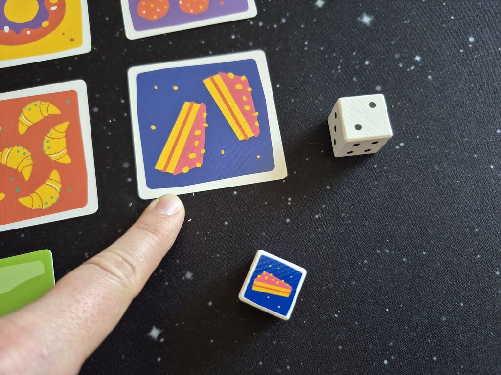 Finger zeigt auf Karte, daneben zwei Würfel.