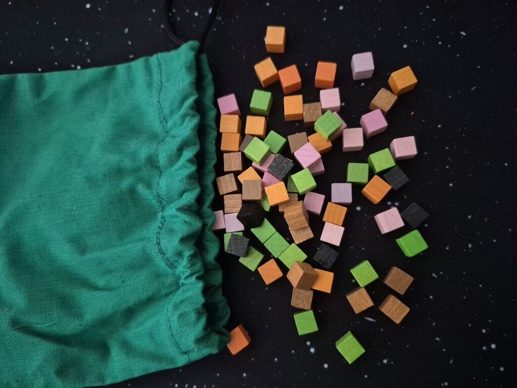 Bunte Holzwürfel neben grünem Stoffbeutel.