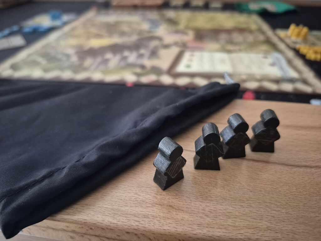 Vier schwarze Meeple neben schwarzem Beutel aus "Village".