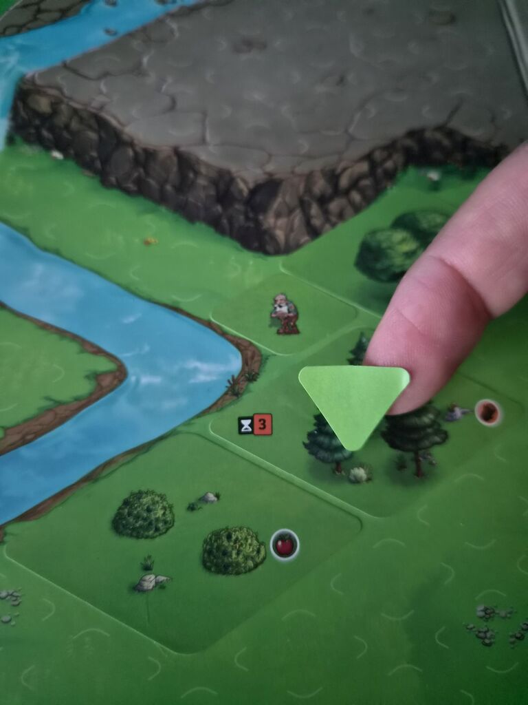 Finger mit dreieckigem Aufkleber über Spielplan von "Cozy Stickerville".