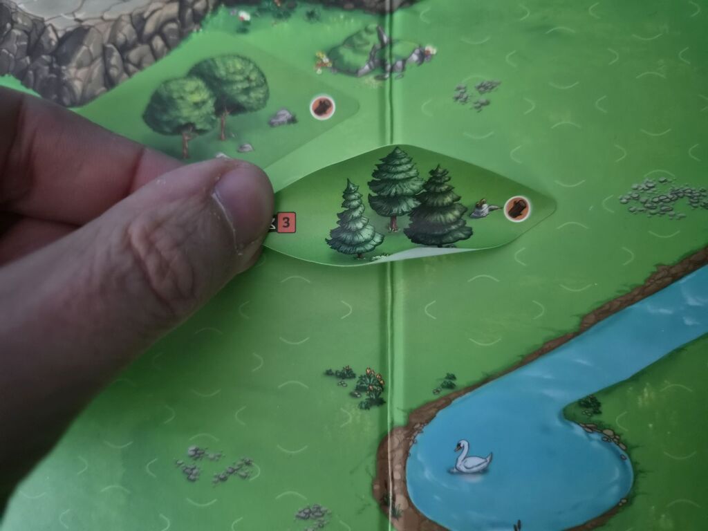 Hand hält Aufkleber über Spielplan.
