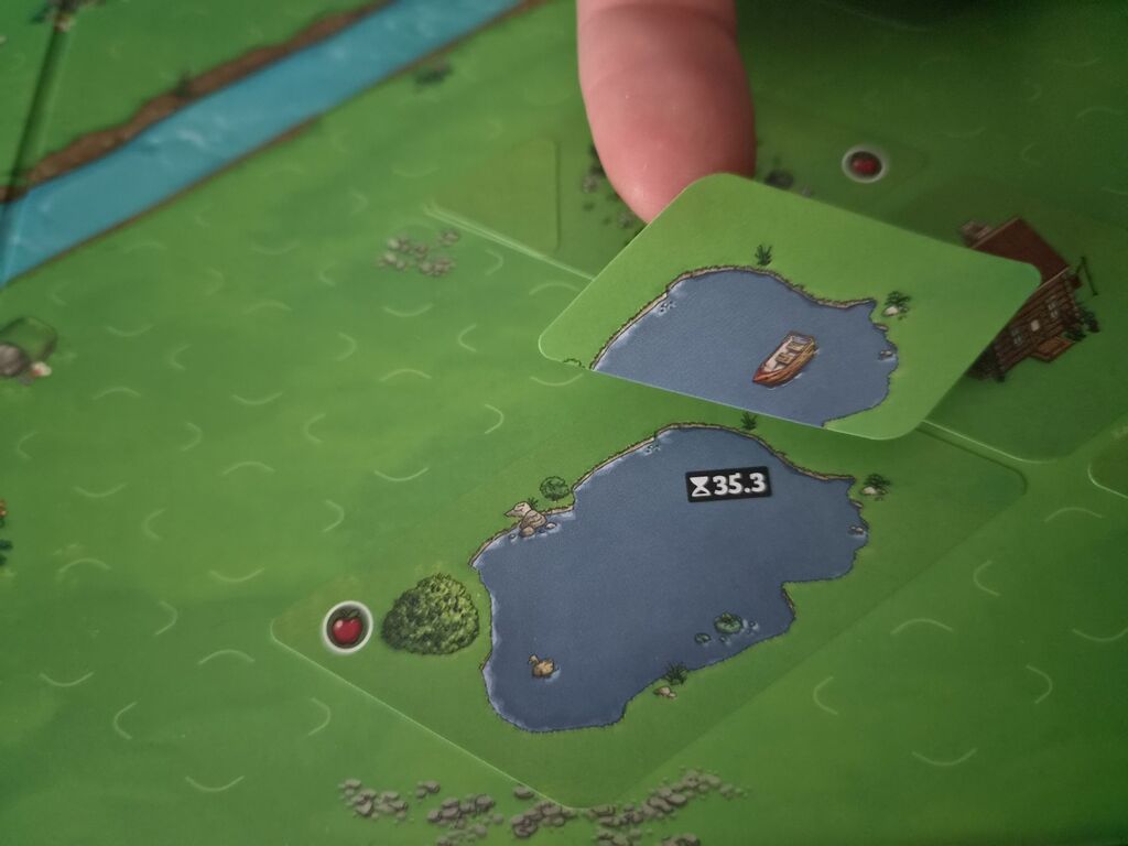 Finger hält Aufkleber über Spielplan mit Aufkleber von "Cozy Stickerville".