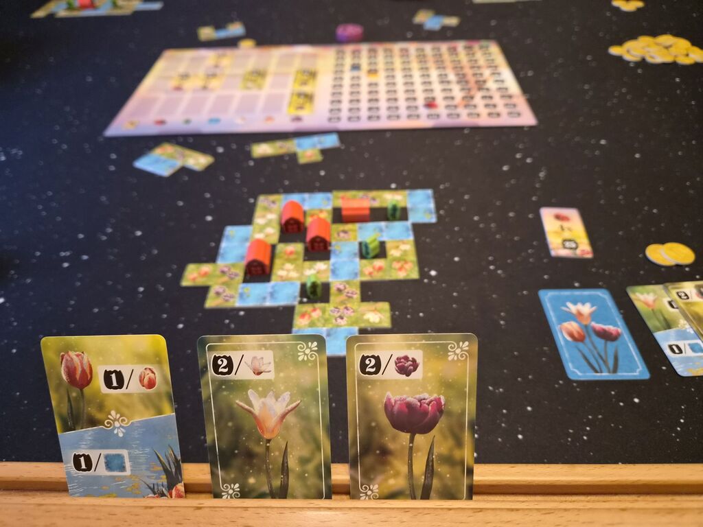 Drei Karten, Spielmaterial im Hintergrund.