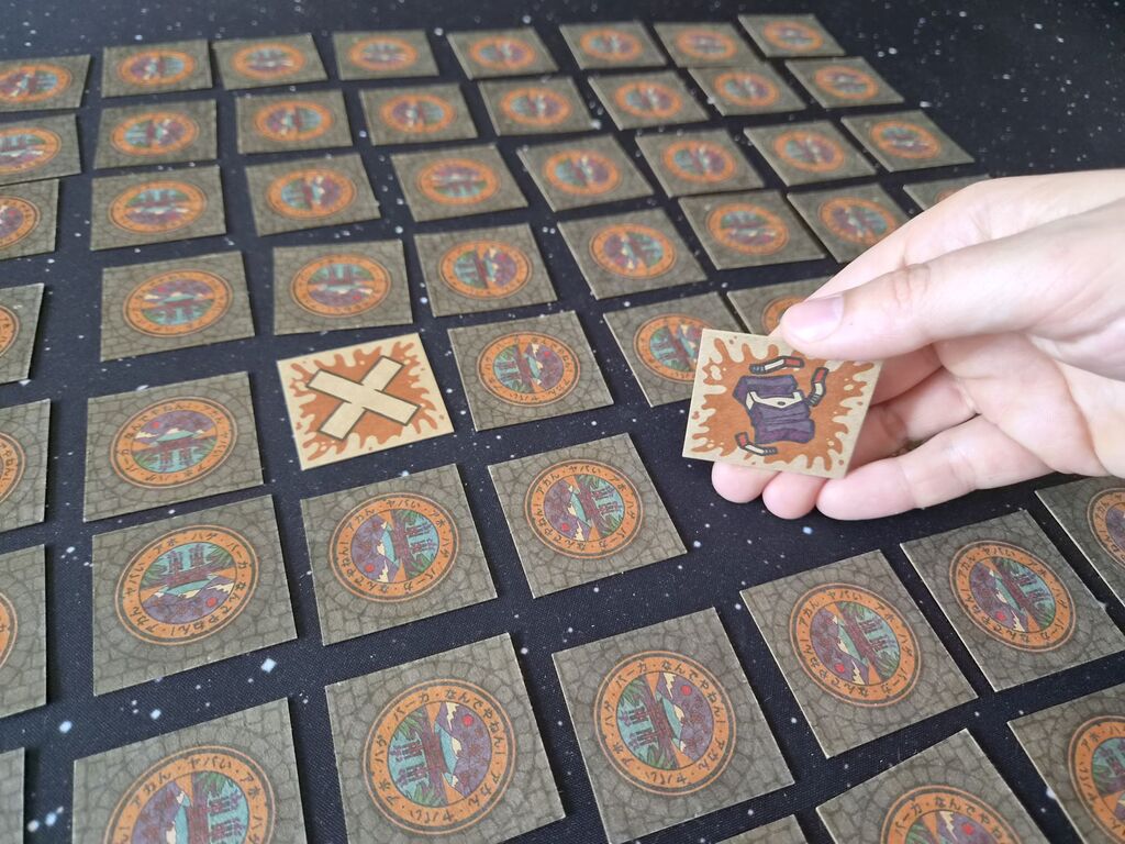 Eine Hand deckt ein Plättchen auf.