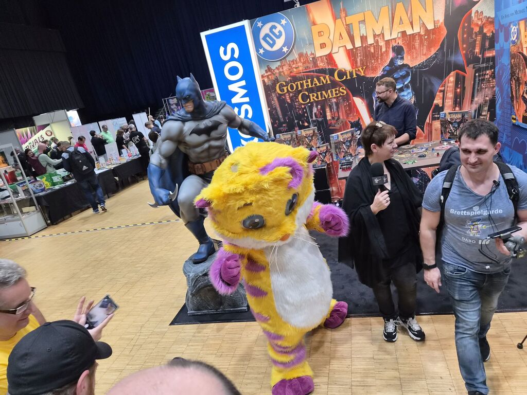 Mensch in Katzenkostüm vor Batman-Figur.