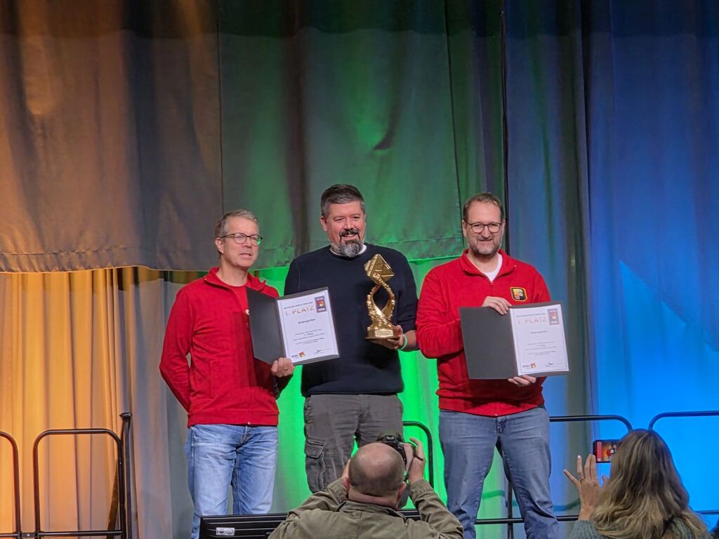 Drei Männer mit Urkunden und einem Pokal.