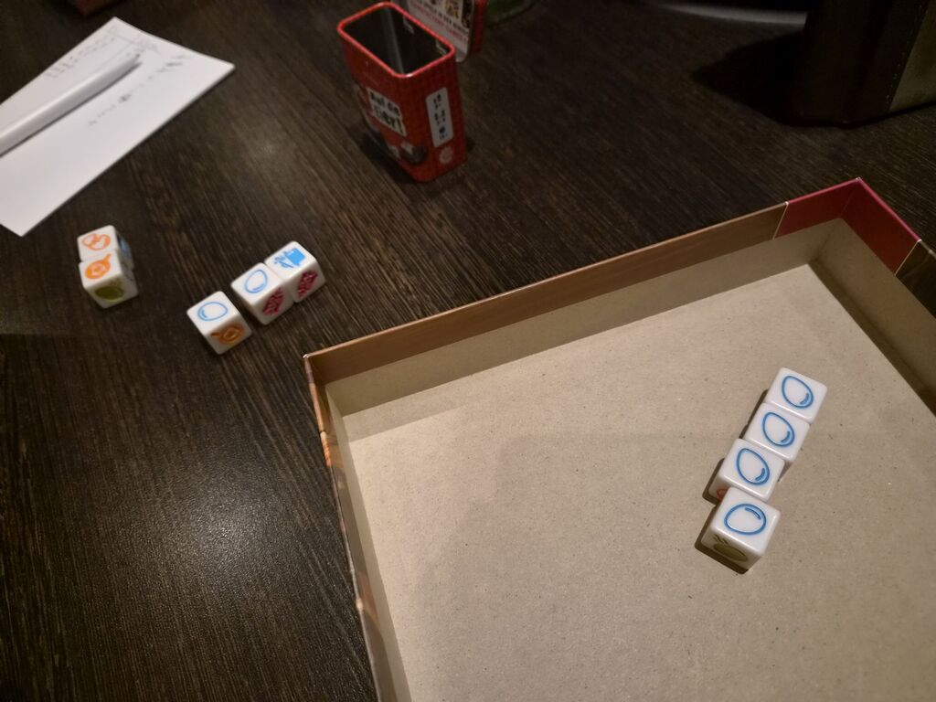 Würfel in Spielschachtel und auf Tisch.