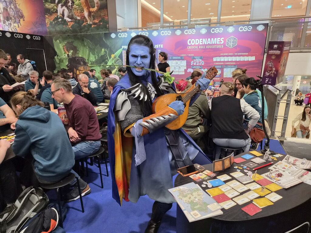 Blau geschminkter Mann in Cosplay-Outfit mit Rose im Mund und Laute.