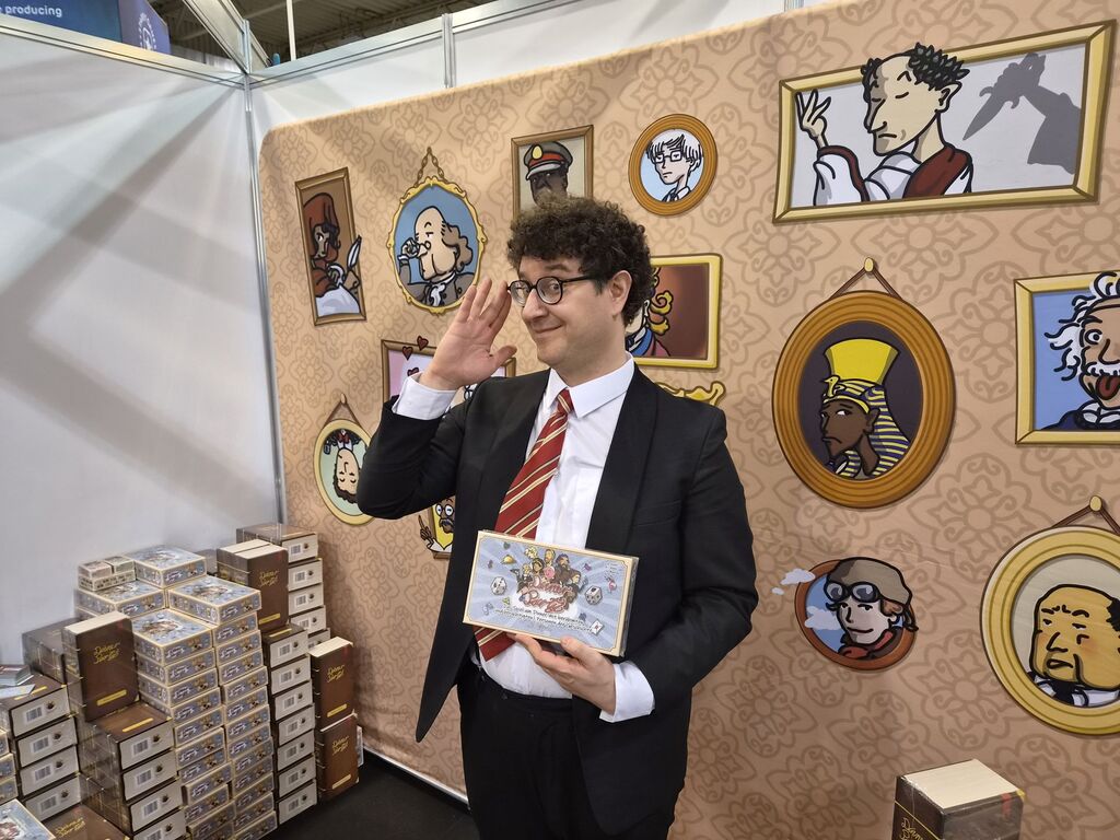 Mann mit Anzug und Krawatte hält Spiel an Messestand bei SPIEL 2026.